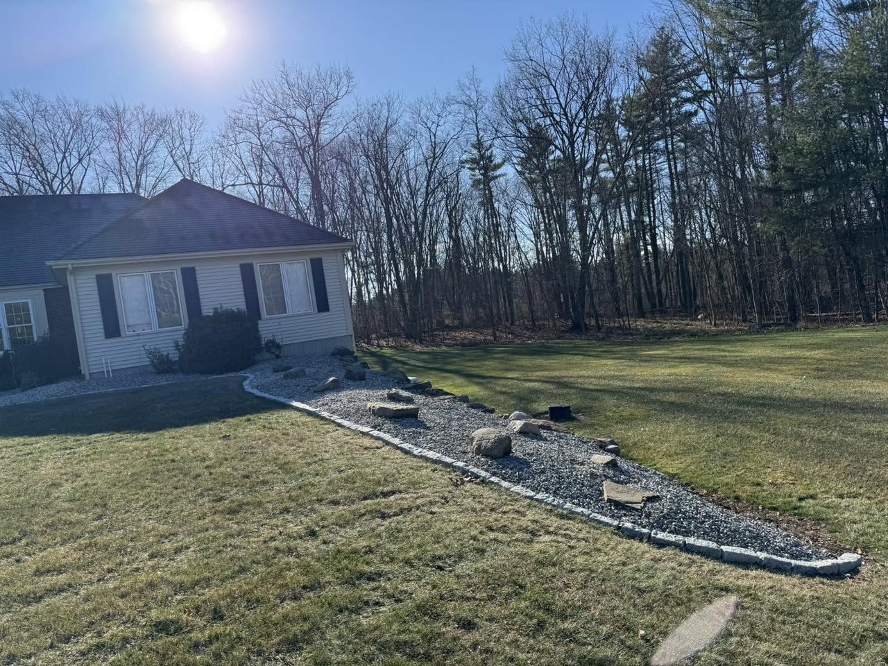 A dry river-rock drainage bed with boulders and cobblestone edging across a sunny lawn