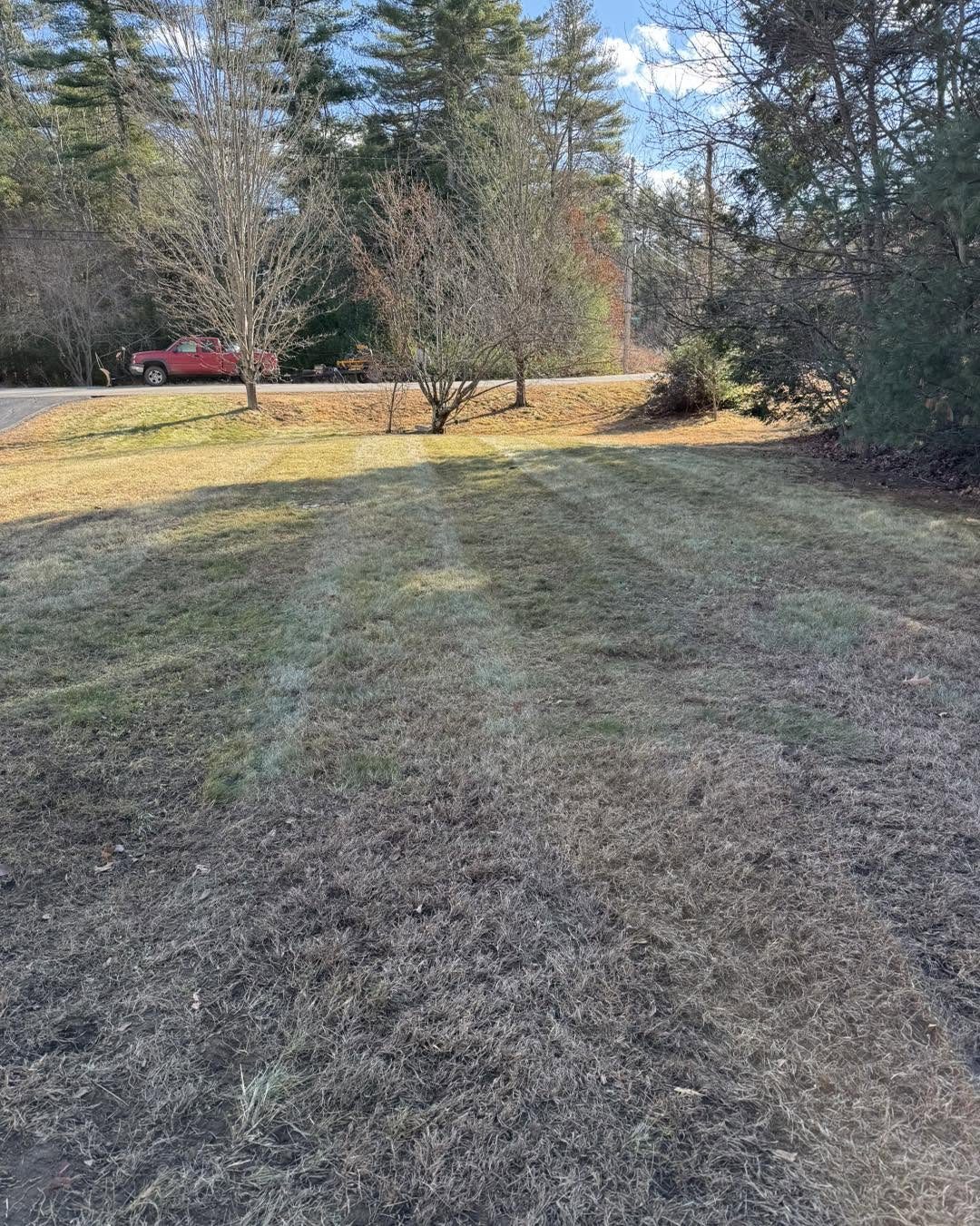 A front lawn raked and cleaned up along a rural road with a red truck